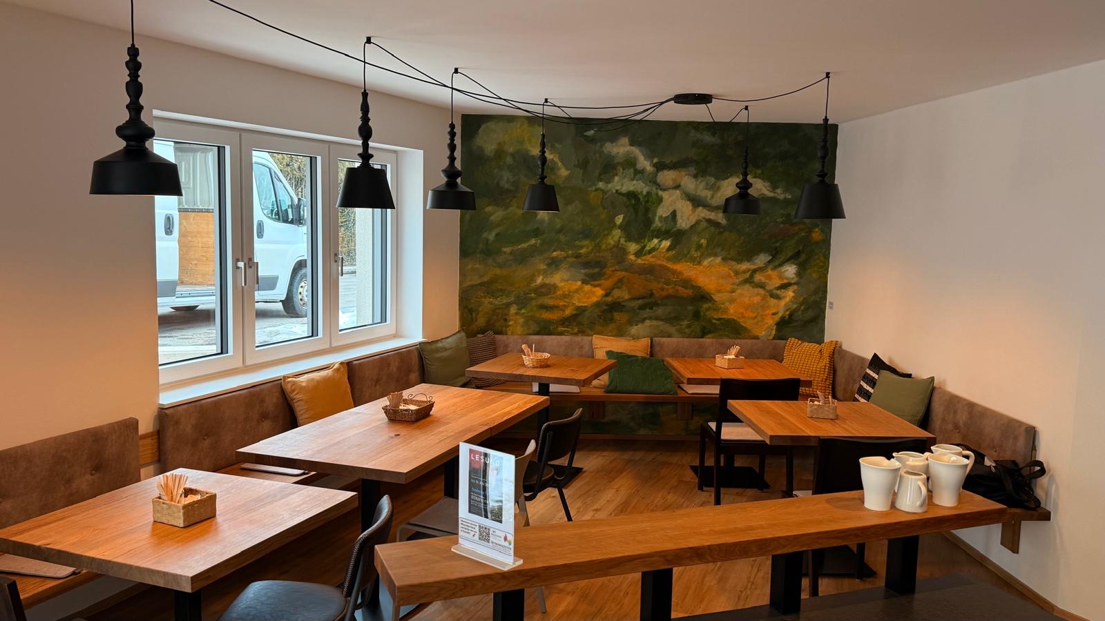 Gemütlicher Gastraum mit Holztischen und grünem Wandbild im Café in der hofmarkt, Taiskirchen